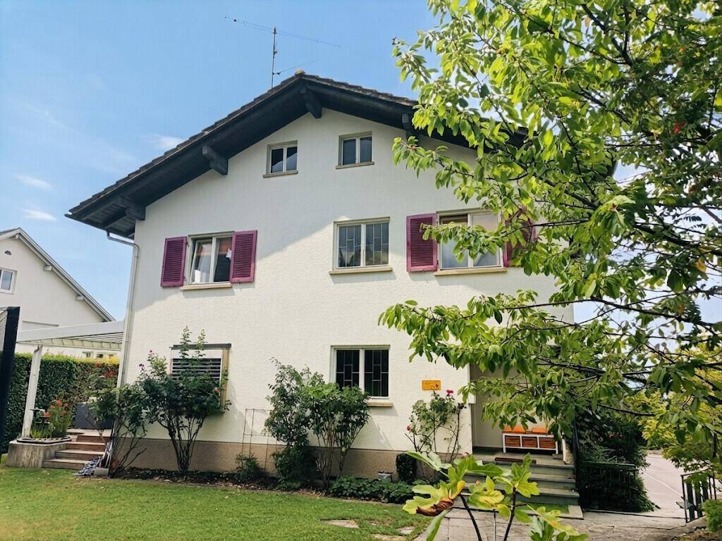 Freistehendes Haus mit traditionellen roten Fensterläden und üppiger Bepflanzung im Garten.