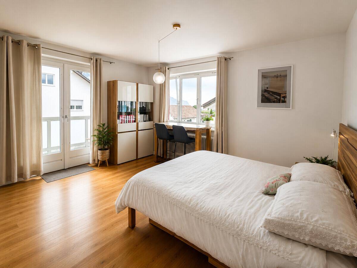 Helles Schlafzimmer mit Holzboden, Doppelbett und Zugang zu einem französischen Balkon.