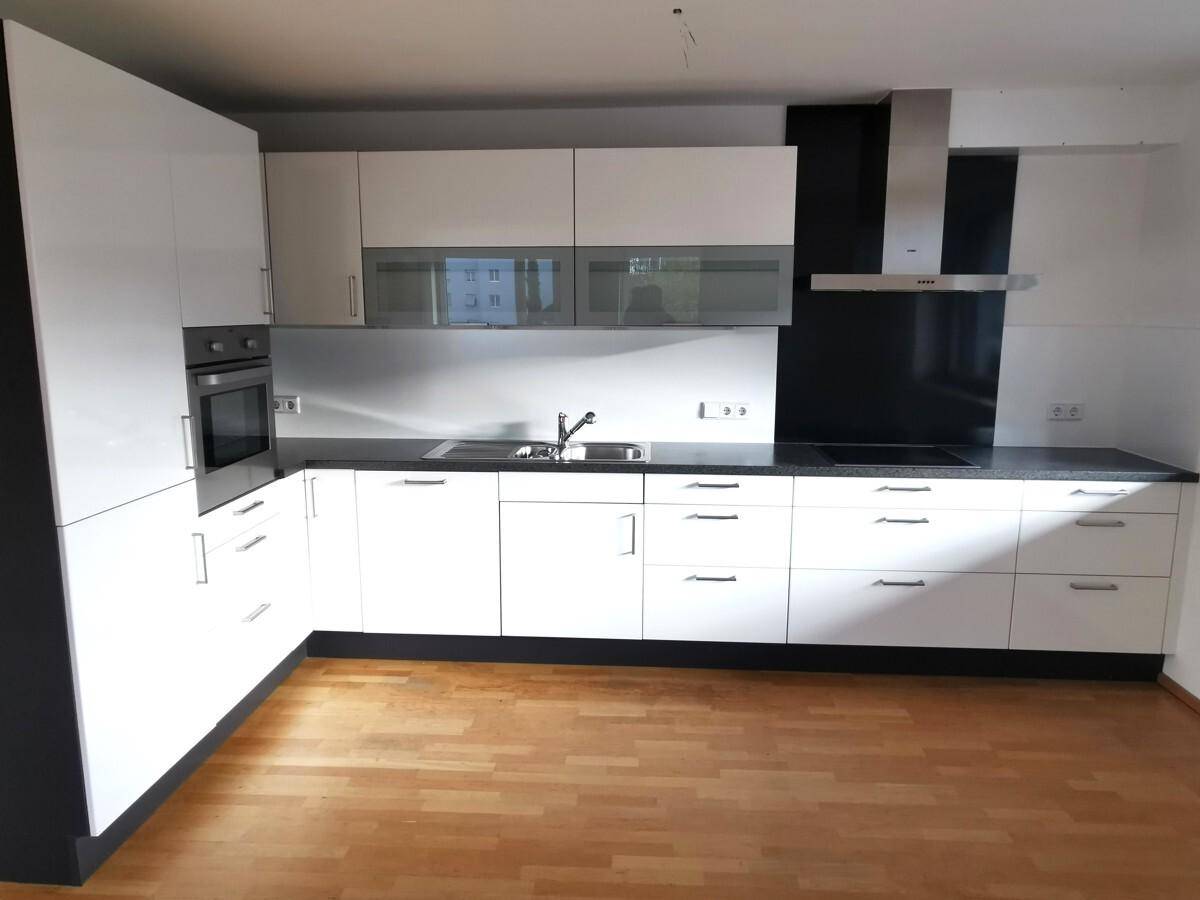 Einbauküche mit weißen Hochglanzfronten, integriertem Backofen und Dunstabzugshaube.