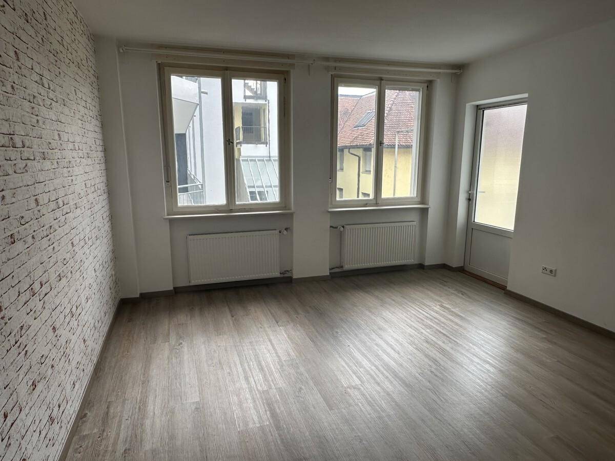 Leerer Raum mit Laminatboden, einer Ziegelwand und Fenstern, die viel Licht hereinlassen.