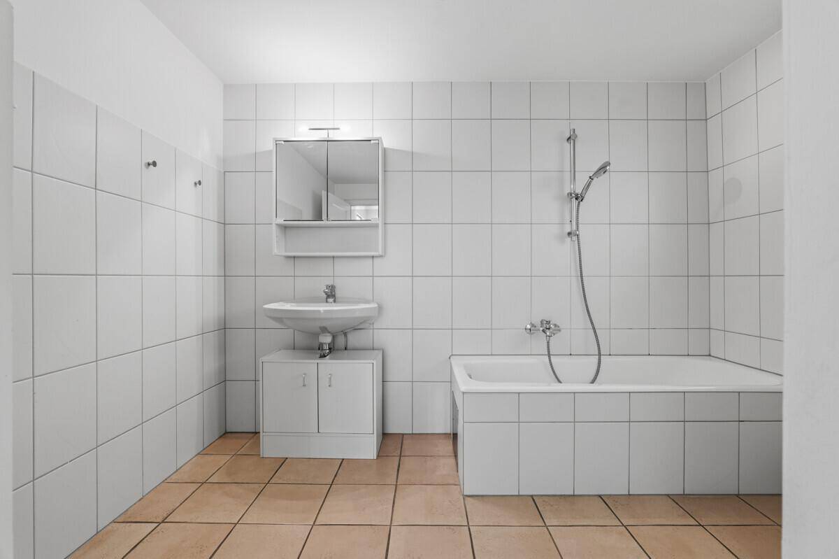 Badezimmer mit weißen Wandfliesen, Badewanne und einem einzelnen Waschbecken mit Spiegelschrank.