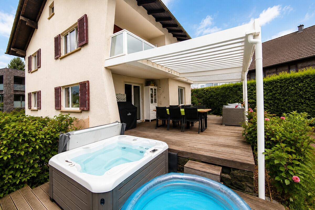 Großzügige Holzterrasse mit Whirlpool, überdachtem Essbereich und gemütlicher Lounge-Ecke.