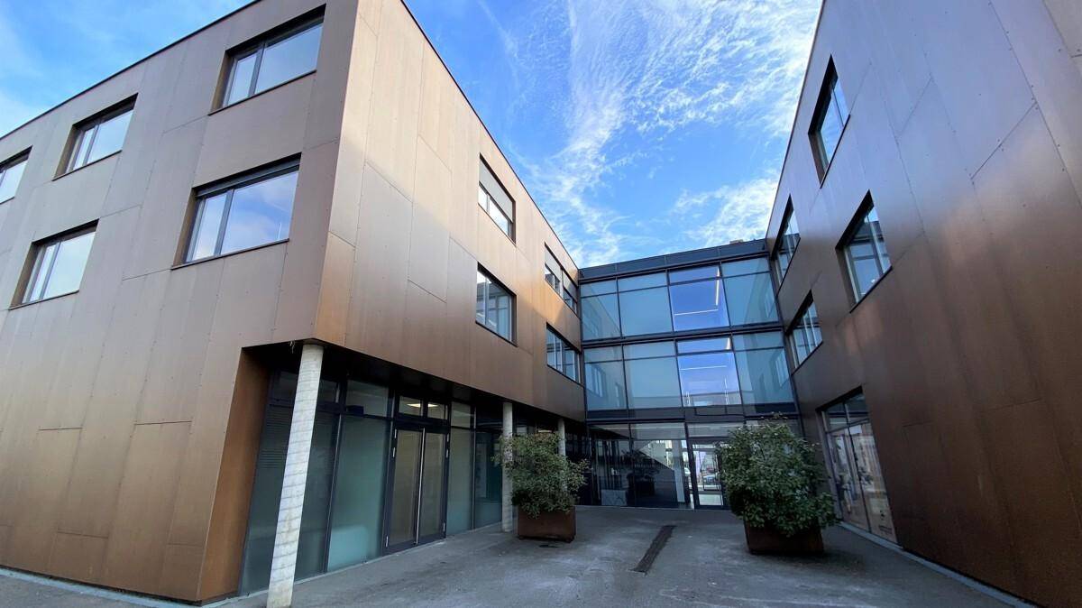 Moderne Gebäudefassade mit braunen Paneelen und großen Glasflächen, die einen Innenhof umschließen.