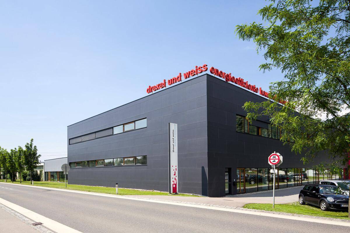Modernes Geschäftsgebäude mit dunkler Fassade und roten Akzenten, umgeben von Bäumen und einer Straße.