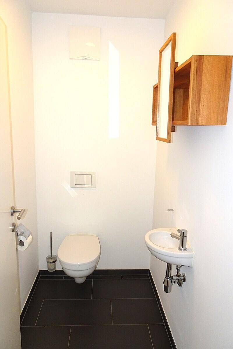 Kleines Gäste-WC mit wandhängender Toilette, Handwaschbecken und dunklen Bodenfliesen.