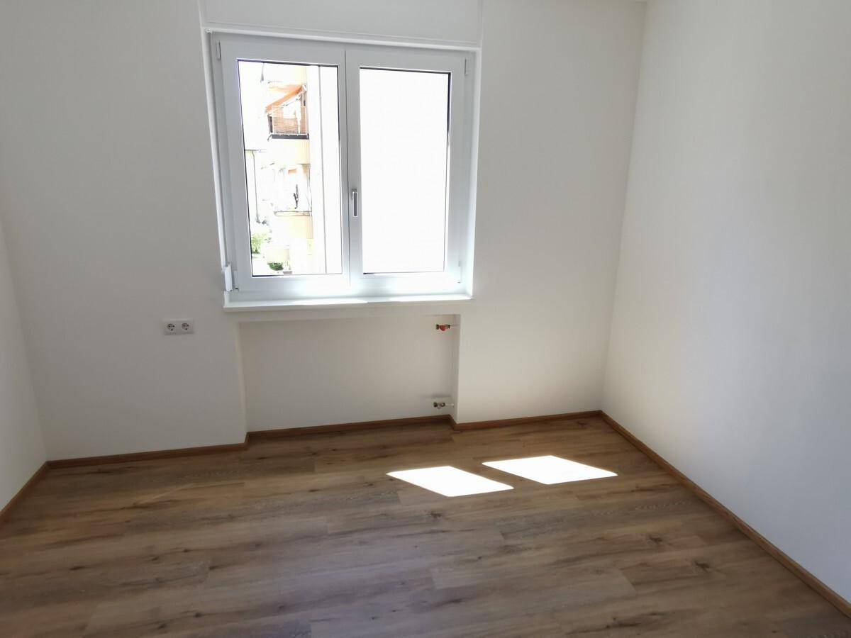 Leeres Zimmer mit Laminatboden und einem Fenster, das den Raum gut belichtet.