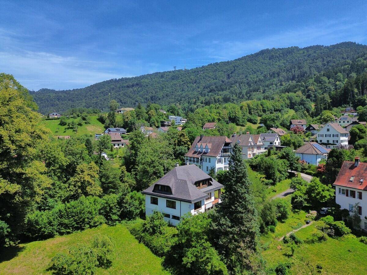 Luftaufnahme des Hauses eingebettet in eine grüne Hügellandschaft mit weiteren Gebäuden.