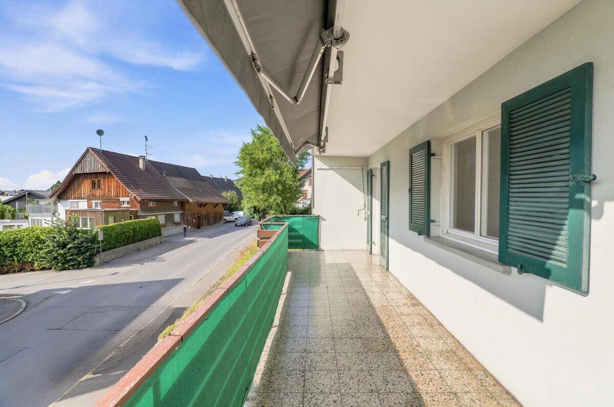 Langer Balkon mit Markise und Blick auf die Straße und die umliegenden Häuser.