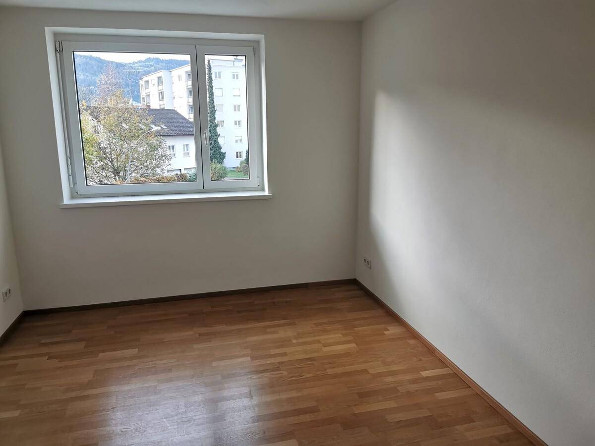Geräumiges Zimmer mit Parkettboden und großem Fenster, das viel Tageslicht hereinlässt.