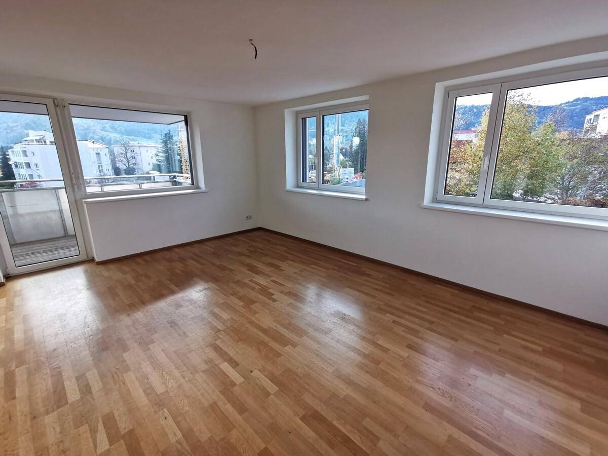 Helles Wohnzimmer mit Parkettboden, großen Fenstern und Zugang zu einem Balkon mit Bergblick.