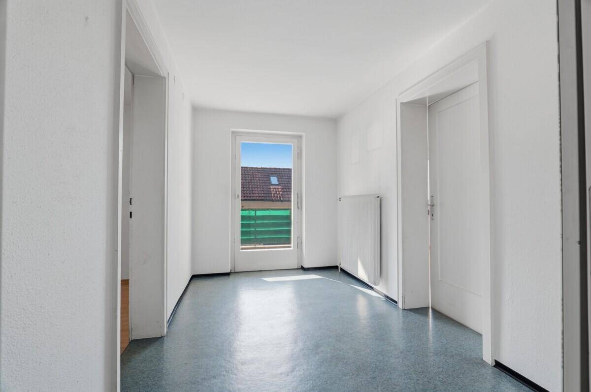 Heller Flur mit Vinylboden und einer Tür, die zu einem Balkon führt.