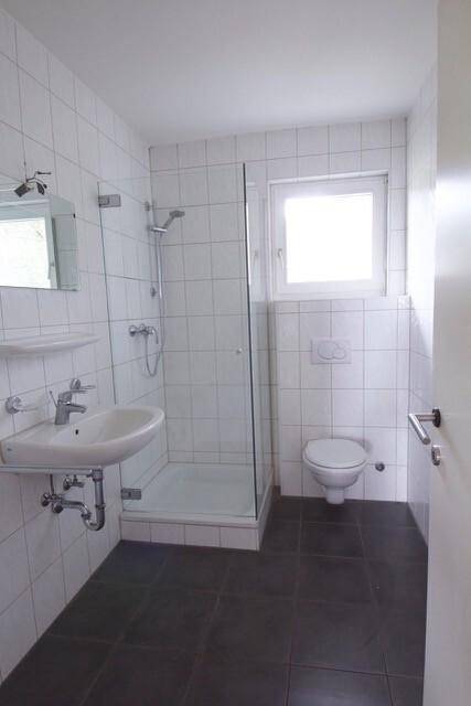 Modernes Badezimmer mit weißen Fliesen, Dusche und Fenster für Tageslicht.