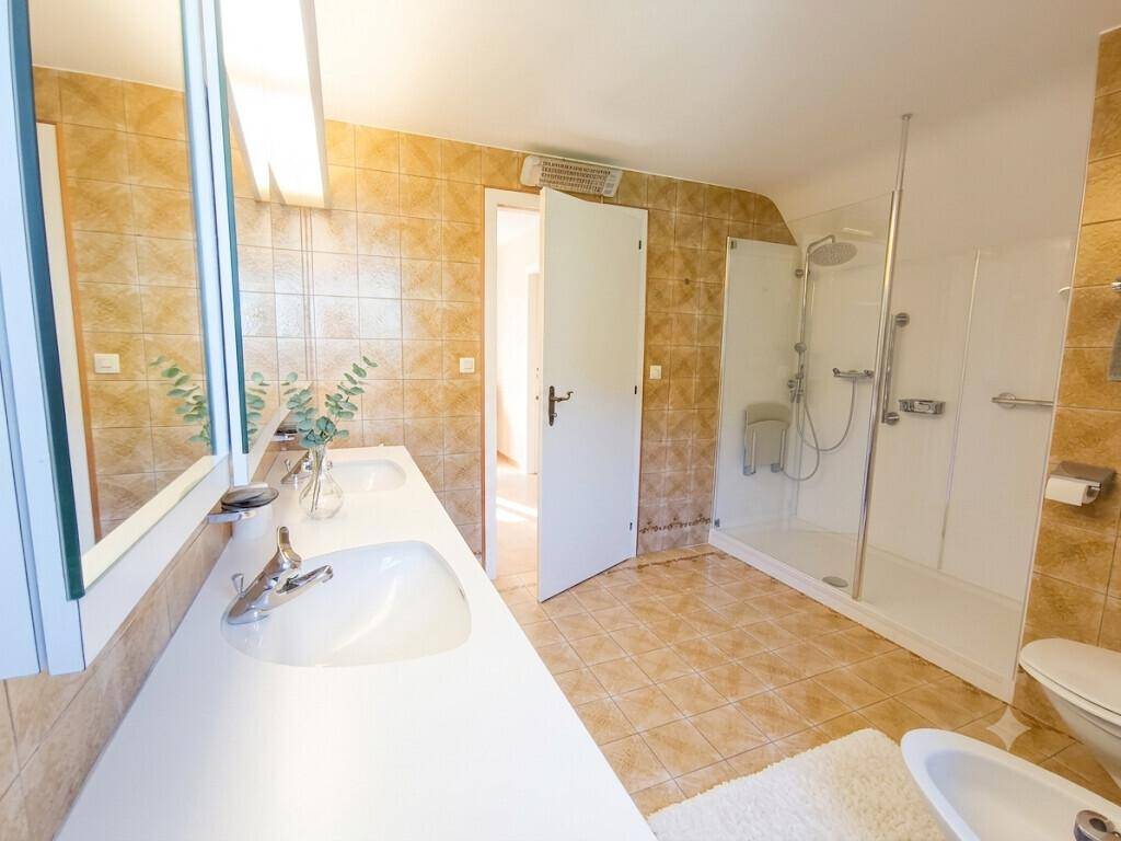 Badezimmer mit Doppelwaschbecken, Dusche, Bidet und braunen Fliesen im 80er-Jahre-Stil.