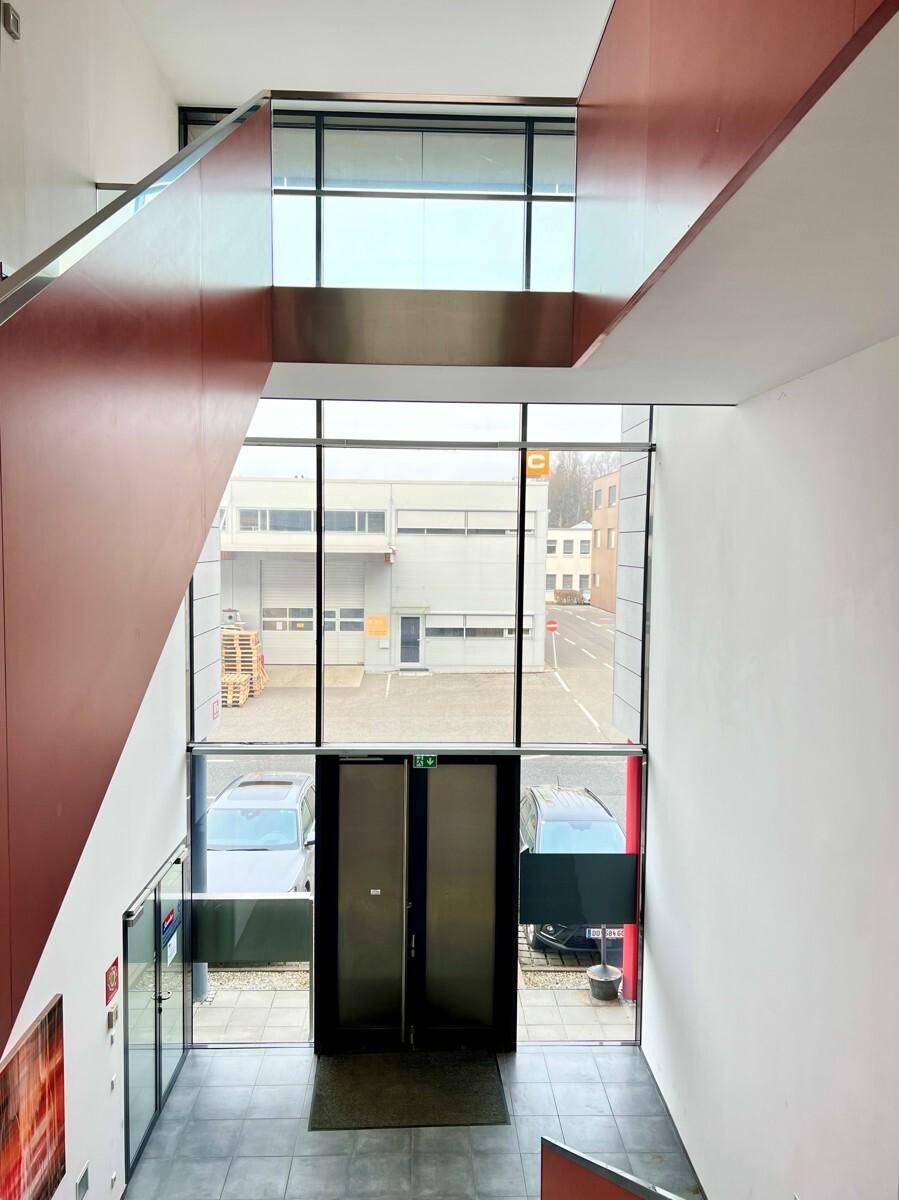 Blick von der Treppe auf den Eingangsbereich mit großer Glasfassade und Blick auf die Straße.