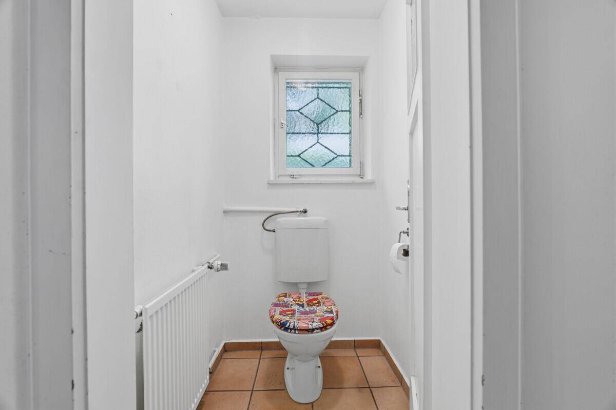 Separate Gästetoilette mit Fenster und Terrakotta-Bodenfliesen, einfach und funktional.