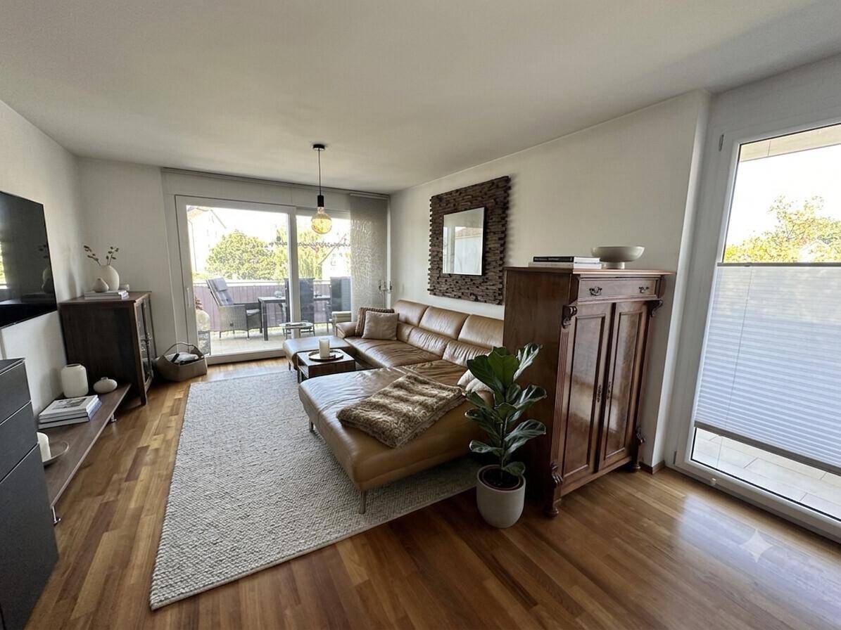 Gemütliches Wohnzimmer mit Ledersofa, Holzboden und Zugang zu einem sonnigen Balkon.