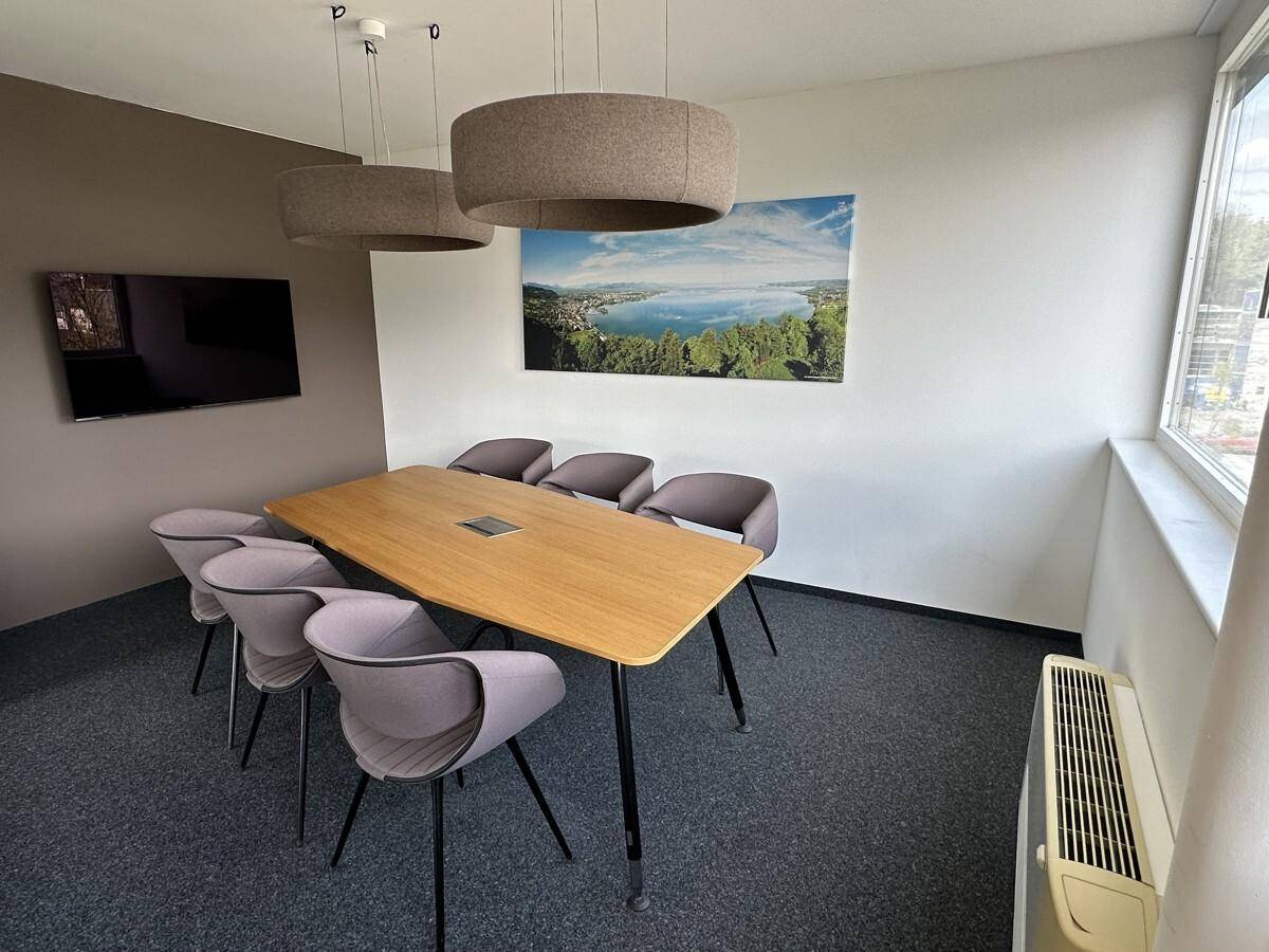 Konferenzraum mit modernem Holztisch, bequemen Stühlen, Wandfernseher und Blick auf die Umgebung.