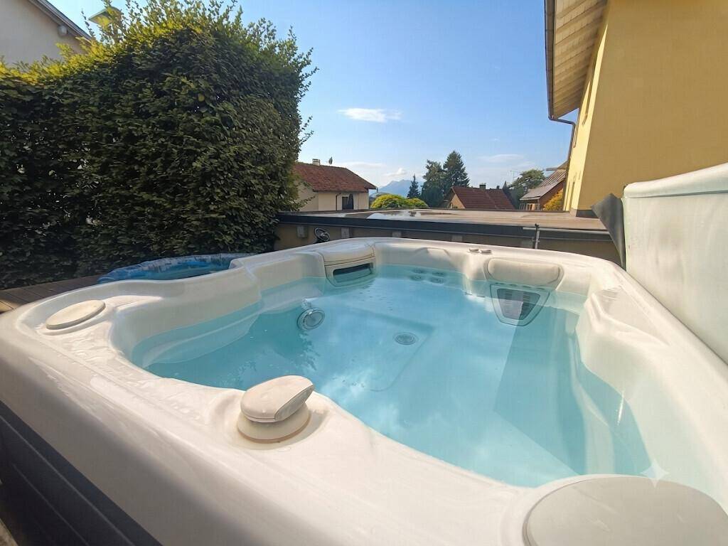 Entspannender Whirlpool auf der Holzterrasse, umgeben von grüner Hecke und mit Bergblick.
