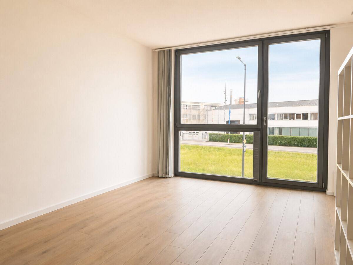 Geräumiger, heller Raum mit Laminatboden und großen Fenstern, die viel Tageslicht hereinlassen.