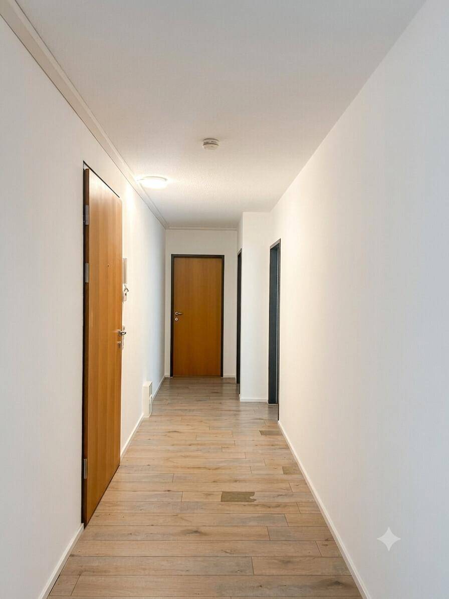 Langer, heller Flur mit Laminatboden und mehreren Türen, der zu den verschiedenen Räumen führt.