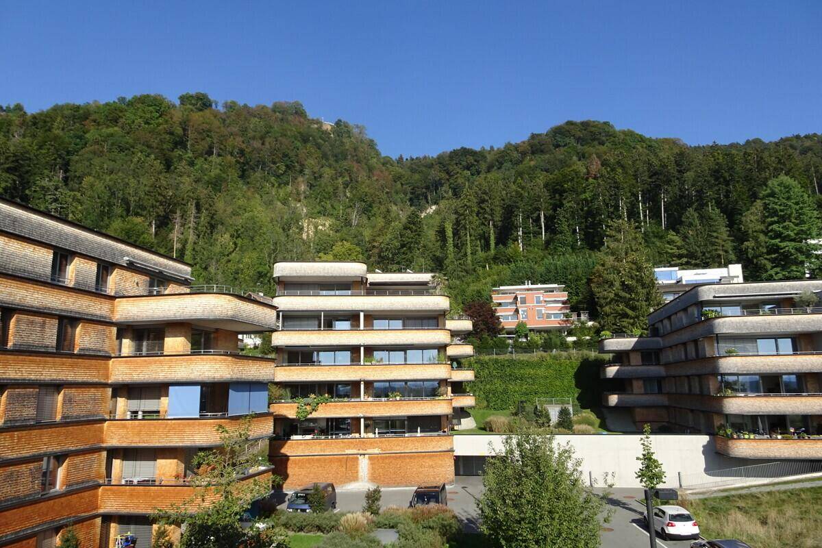 Mehrere moderne Wohngebäude mit Terrassen und grüner Umgebung am Fuße eines bewaldeten Hügels.