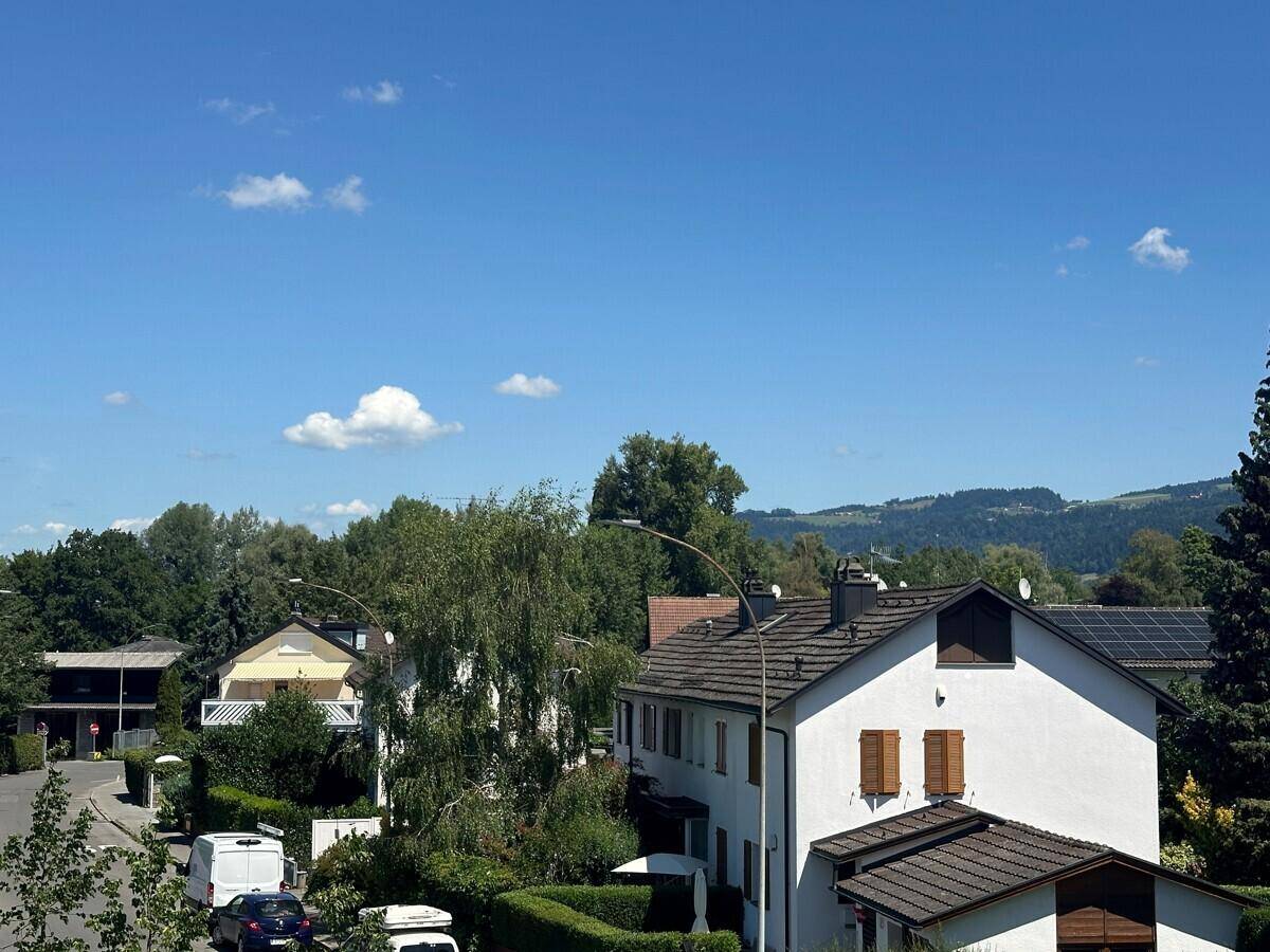 Panoramablick über eine ruhige Wohnsiedlung mit Häusern, Bäumen und grünen Hügeln im Hintergrund.