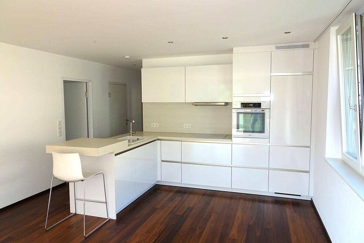 Moderne Einbauküche mit weißen Hochglanzfronten, integrierten Geräten und einer Frühstücksbar.