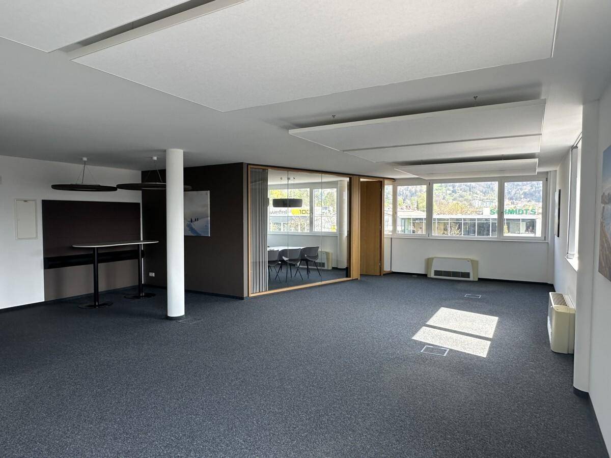 Großzügiger Bürobereich mit Teppichboden, Glaswänden und einem Stehtischbereich, ideal für flexible Arbeitskonzepte.
