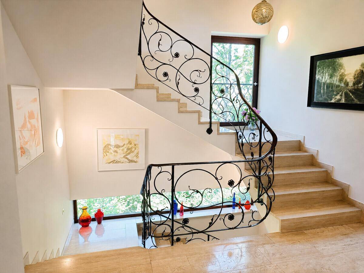 Elegantes Treppenhaus mit schmiedeeisernem Geländer und Natursteinboden, hell und offen gestaltet.
