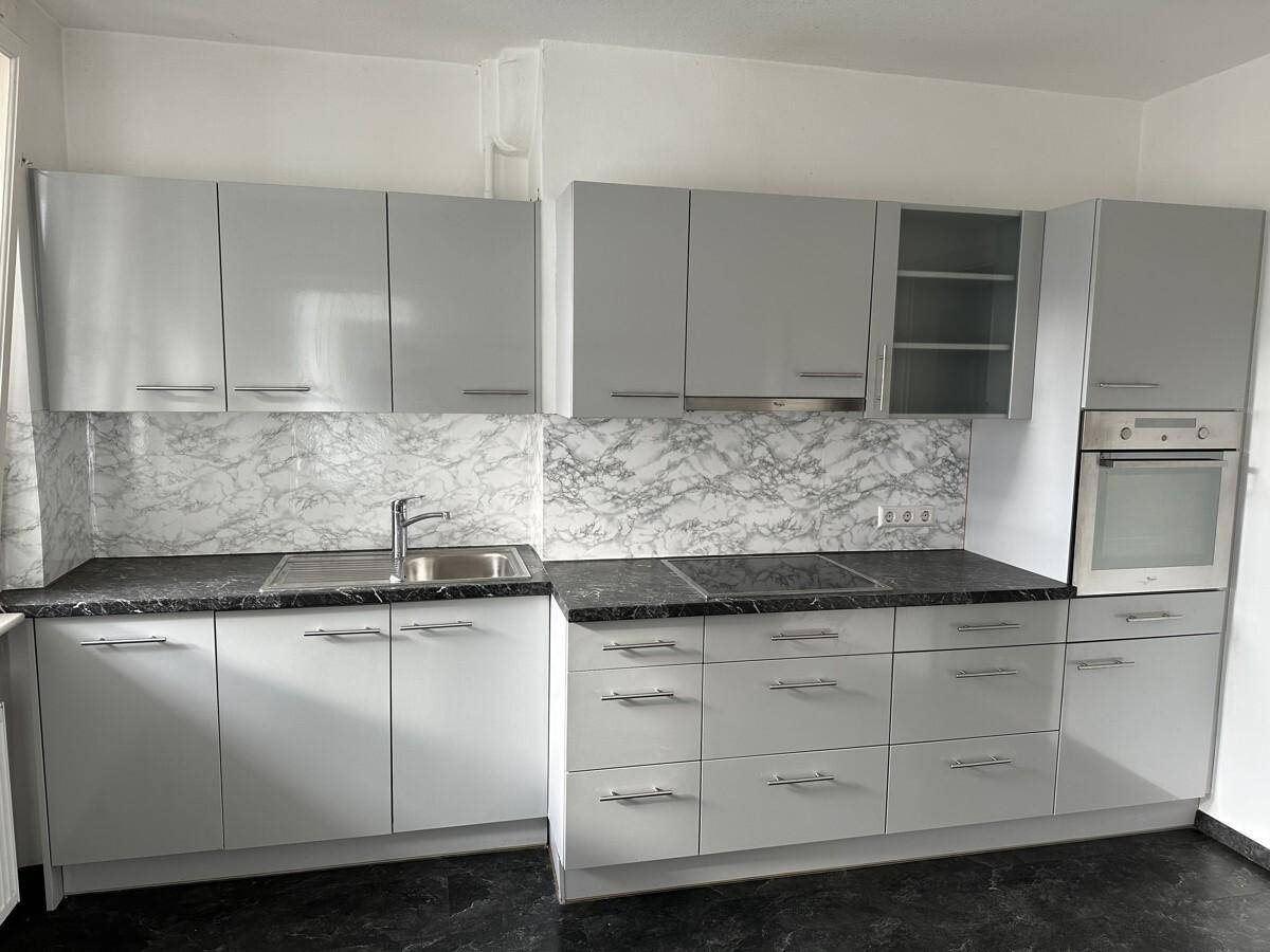 Moderne Einbauküche mit grauen Hochglanzfronten, dunkler Arbeitsplatte und integriertem Backofen.