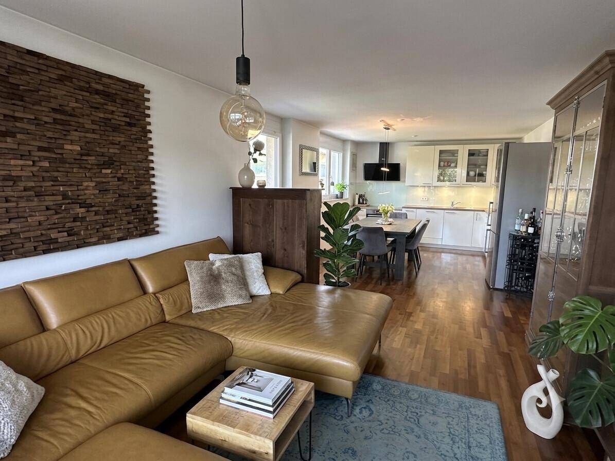 Offener Wohn- und Essbereich mit Ledersofa, Holzboden und Blick auf die moderne Küche.