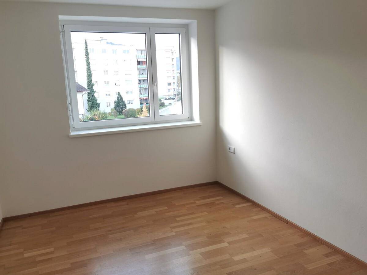 Helles Schlafzimmer mit Parkettboden und einem großen Fenster mit Blick auf die Umgebung.