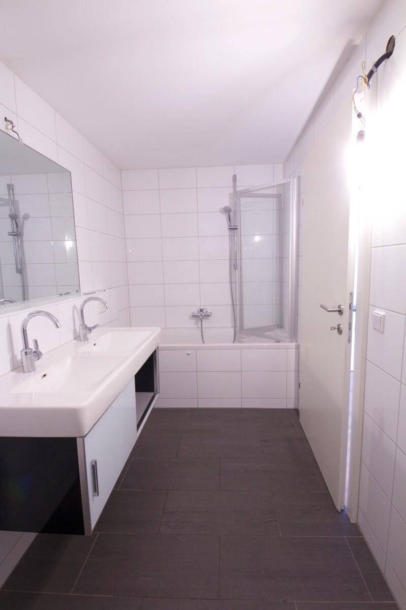 Badezimmer mit Badewanne inklusive Duschwand, Doppelwaschbecken und weißen Wandfliesen.
