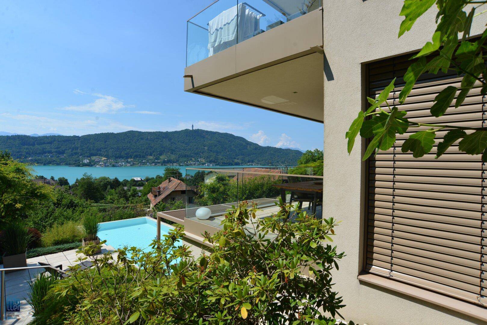 Panoramablick von einem Balkon auf den darunterliegenden Poolbereich und die beeindruckende Seen- und Berglandschaft.