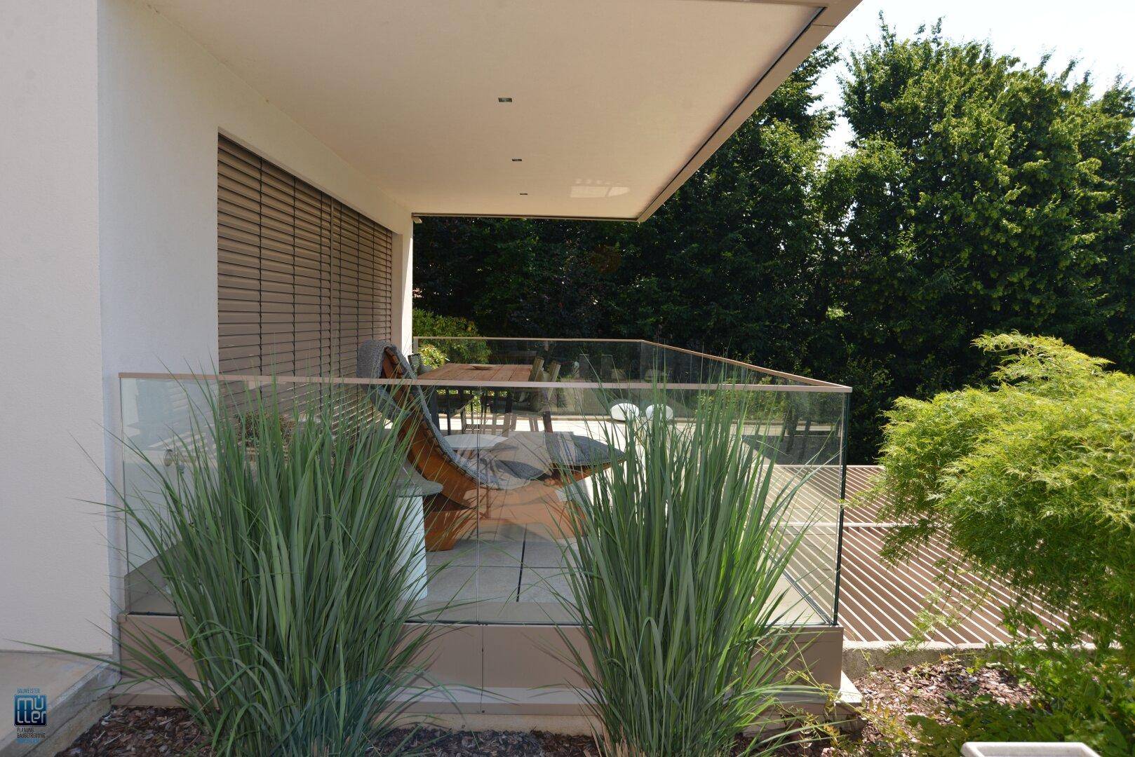 Heller Balkon mit Essbereich und elegantem Glasgeländer, umgeben von üppigem Grün für private Momente.