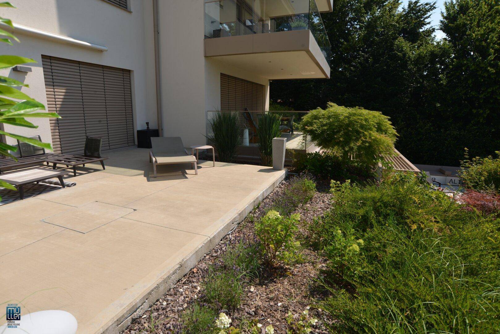 Ebenerdige Terrasse mit Liegestuhl, umgeben von gepflegten Pflanzen und Sträuchern, ideal zum Entspannen.
