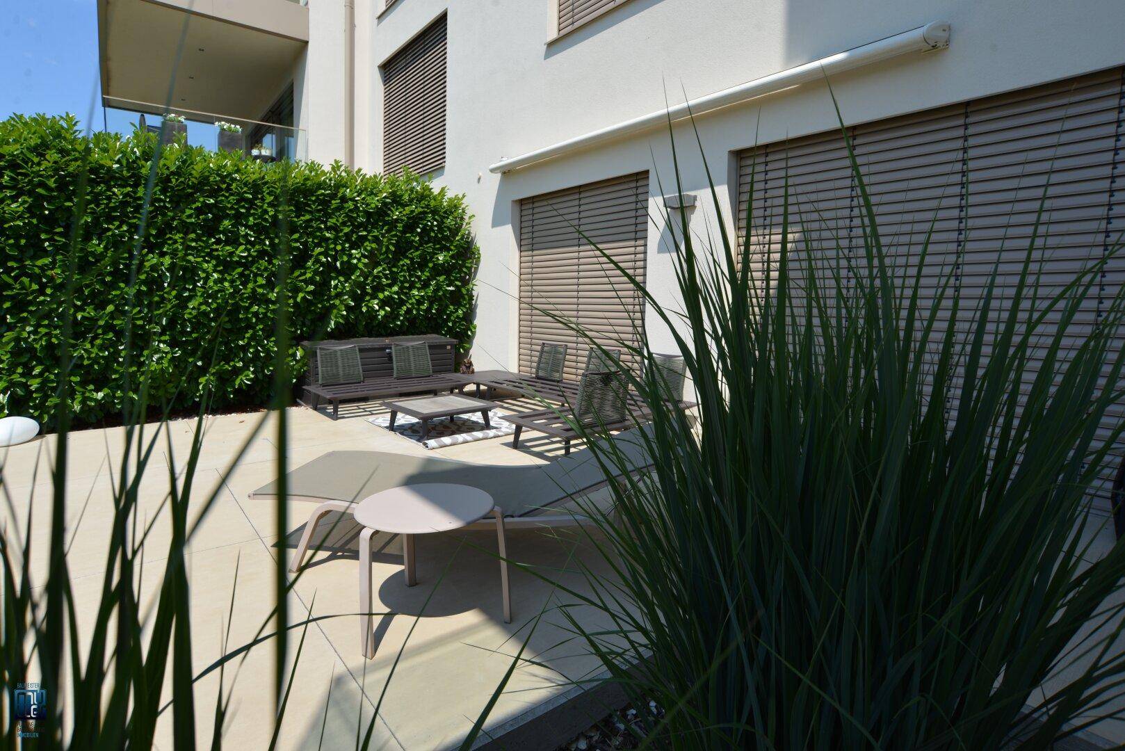 Gemütliche ebenerdige Terrasse mit modernen Gartenmöbeln, umgeben von einer grünen Hecke für Privatsphäre.