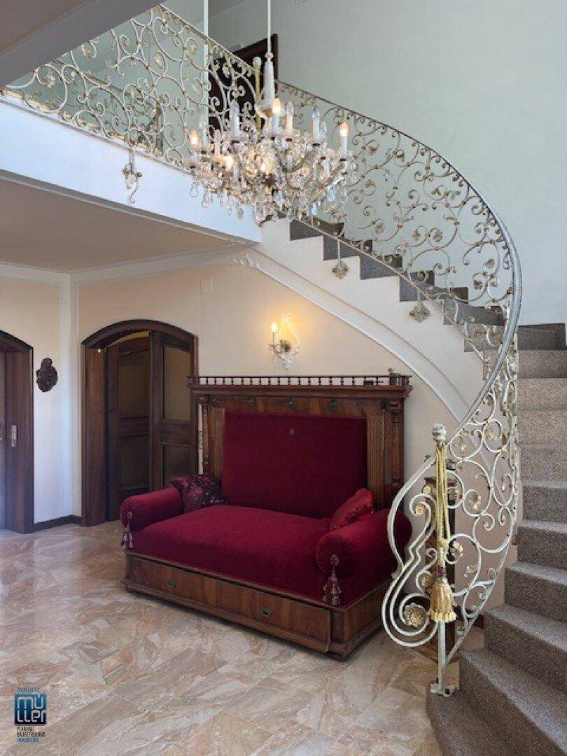 Prunkvoller Eingangsbereich mit geschwungener Treppe, Kronleuchter und einem eleganten Sofa unter der Galerie.