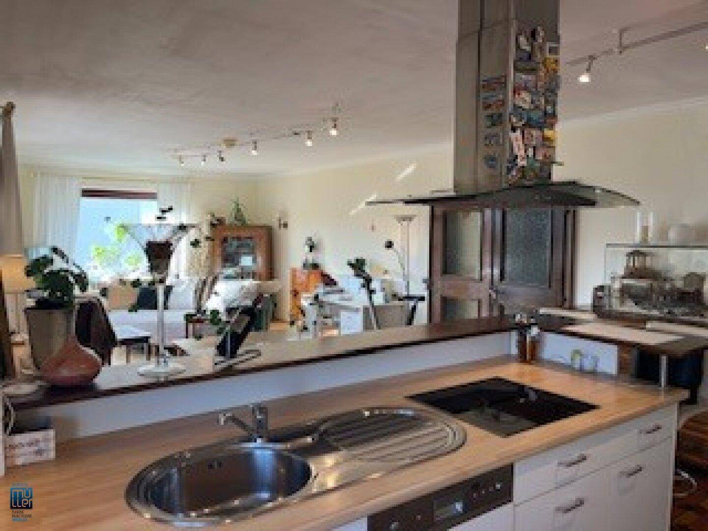 Offener Wohnbereich mit integrierter Küche, Holzboden und viel natürlichem Licht durch große Fenster.