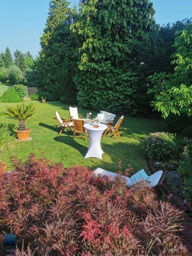 Sonnige Gartenterrasse mit bequemen Sitzgelegenheiten und üppiger, grüner Bepflanzung für entspannte Stunden.