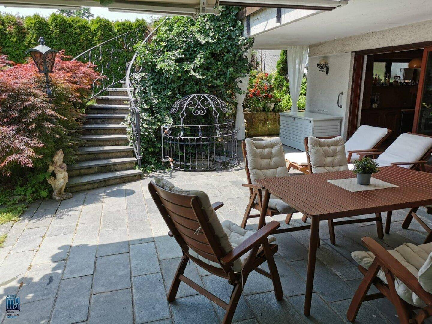 Attraktive Terrasse mit Essbereich, dekorativer Treppe und üppiger, grüner Bepflanzung.