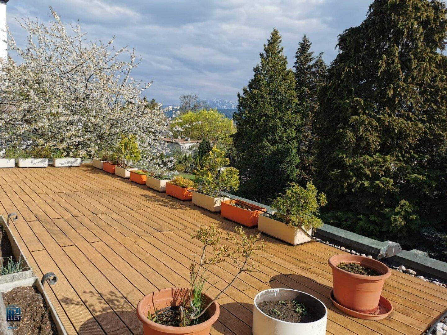 Große Dachterrasse mit Holzboden, dekorativen Pflanzenkübeln und einem weiten Blick auf die Landschaft.
