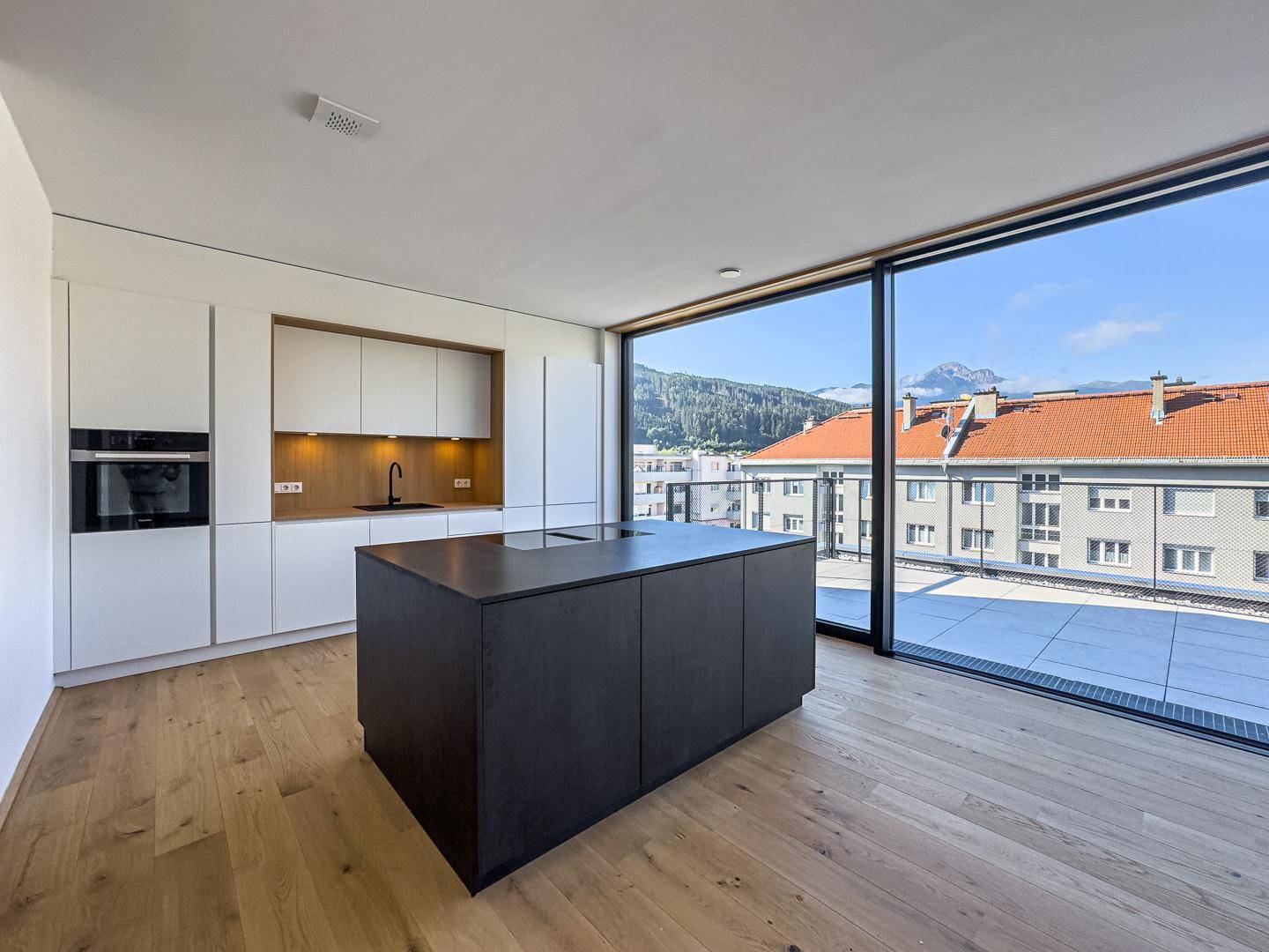 Moderne Küche mit dunkler Kücheninsel, weißen Schränken und großen Fenstern mit Bergblick.
