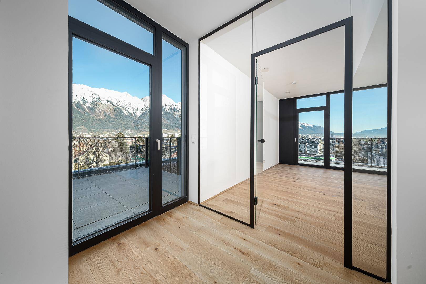 Heller Flur mit Holzboden, modernen Glastüren und Blick auf die schneebedeckten Berge.