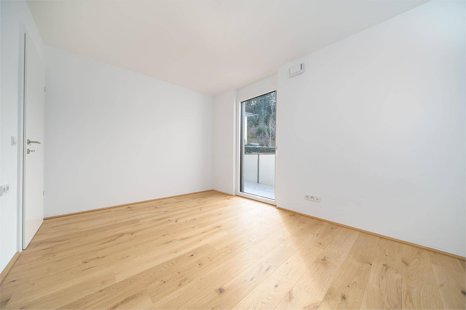 Helles Zimmer mit Parkettboden und Zugang zu einem kleinen Balkon, ideal als Schlafzimmer.