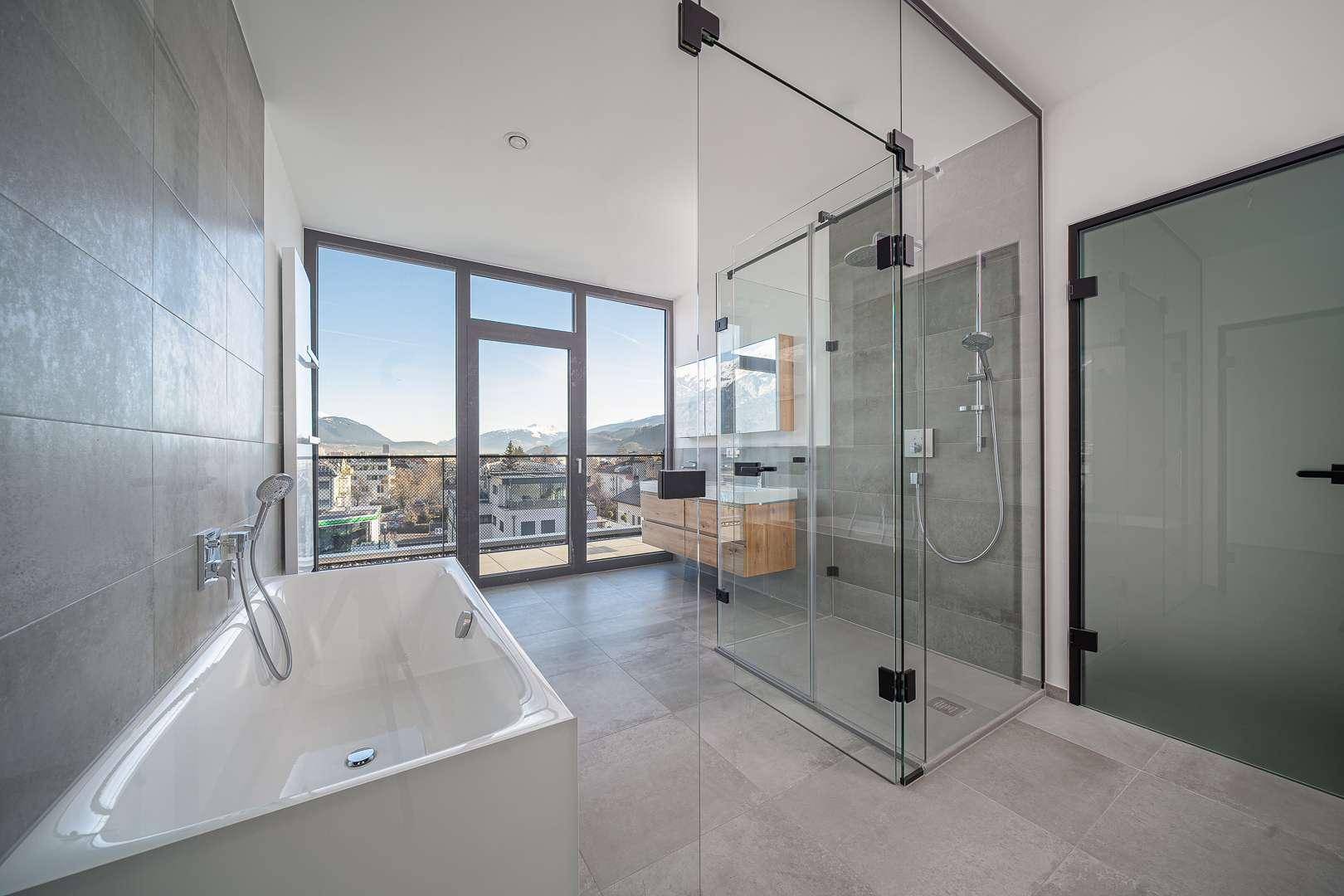 Modernes Badezimmer mit Badewanne, begehbarer Dusche und großen Fenstern mit Bergblick.
