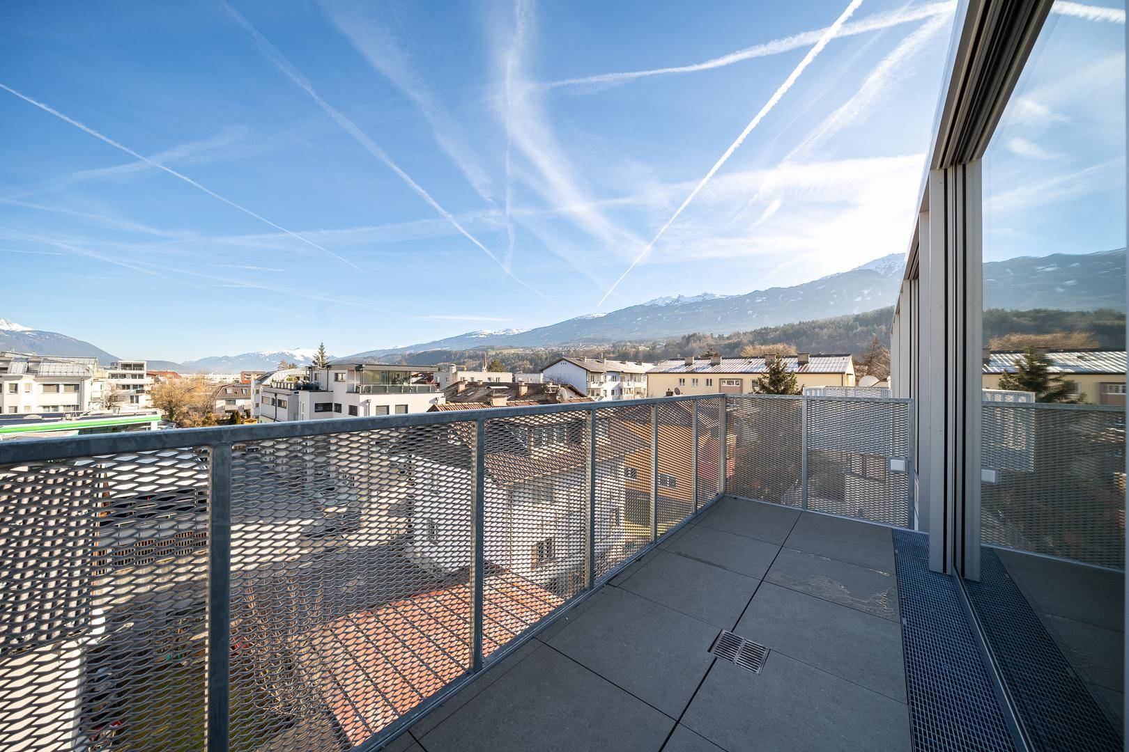 Terrasse mit Metallgeländer und weitem Blick über die Stadt und die schneebedeckten Berge.