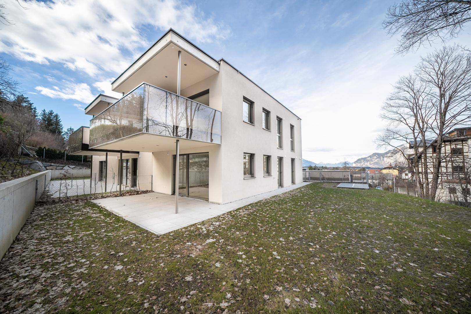 Moderne Wohnanlage mit Terrasse, Rasenfläche und Blick auf die Berge.