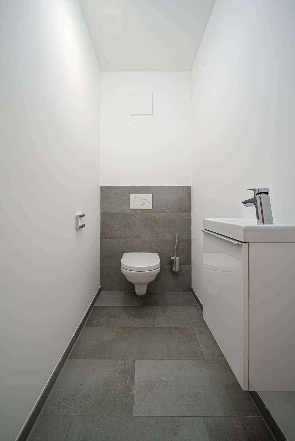 Kleines, modernes Gäste-WC mit Wand-WC, Waschbecken und grauen Fliesen.