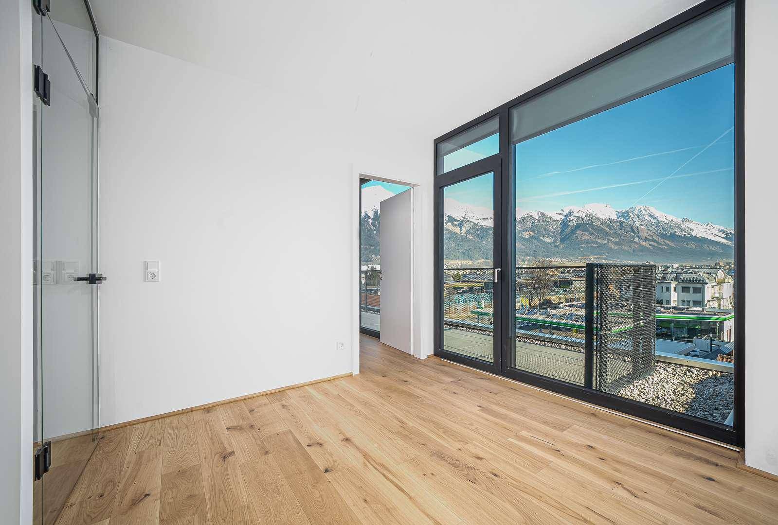 Geräumiges Schlafzimmer mit Holzboden und Panoramafenstern, die einen weiten Blick bieten.